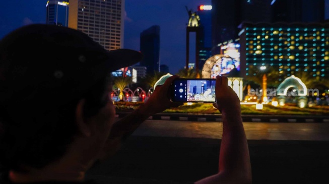 Warga memoto dekorasi lebaran di kawasan Bundaran Hotel Indonesia, Jakarta, Senin (8/4/2024). [Suara.com/Alfian Winanto]