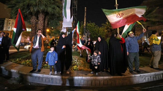 Demonstran mengibarkan bendera Iran dan bendera Palestina saat mereka berkumpul setelah Iran melancarkan serangan drone dan rudal ke Israel di Lapangan Palestina di Teheran, Iran, Minggu (14/4/2024). [ATTA KENARE / AFP]