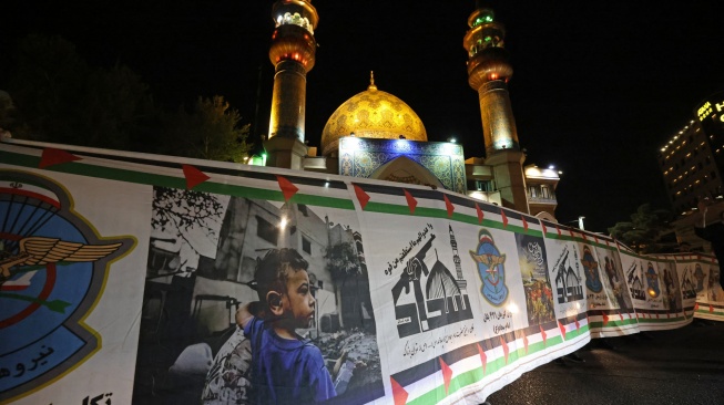 Demonstran mengibarkan bendera Iran dan bendera Palestina saat mereka berkumpul setelah Iran melancarkan serangan drone dan rudal ke Israel di Lapangan Palestina di Teheran, Iran, Minggu (14/4/2024). [ATTA KENARE / AFP]