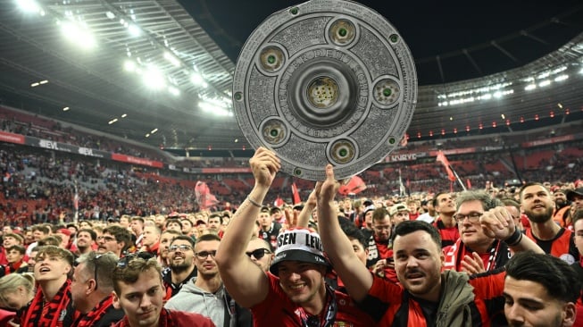 Para suporter Bayer Leverkusen berselebrasi dengan replika trofi Bundesliga setelah pertandingan sepak bola Bundesliga antara Bayer Leverkusen dan Werder Bremen di Leverkusen, Jerman barat, Minggu (14/4/2024). [INA FASSBENDER / AFP]