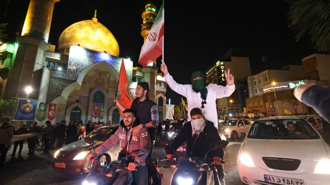 Demonstran mengibarkan bendera Iran dan bendera Palestina saat mereka berkumpul setelah Iran melancarkan serangan drone dan rudal ke Israel di Lapangan Palestina di Teheran, Iran, Minggu (14/4/2024). [ATTA KENARE / AFP]