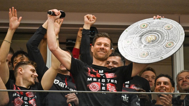 Pelatih Bayer Leverkusen, Xabi Alonso selebrasi dengan replika trofi Bundesliga bersama para pemainnya setelah pertandingan sepak bola Bundesliga antara Bayer Leverkusen dan Werder Bremen di Leverkusen, Jerman barat, Minggu (14/4/2024). [INA FASSBENDER / AFP]