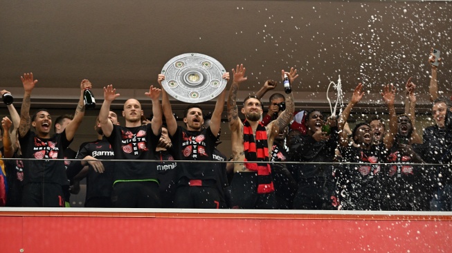 Para pemain Bayer Leverkusen berselebrasi dengan replika trofi Bundesliga setelah pertandingan sepak bola Bundesliga antara Bayer Leverkusen dan Werder Bremen di Leverkusen, Jerman barat, Minggu (14/4/2024). [INA FASSBENDER / AFP]