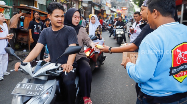 Relawan Jokowi membagikan susu kepada warga yang melintas di wilayah Menteng Wadas Timur, Jakarta, Selasa (30/4/2024). [Suara.com/Alfian Winanto]