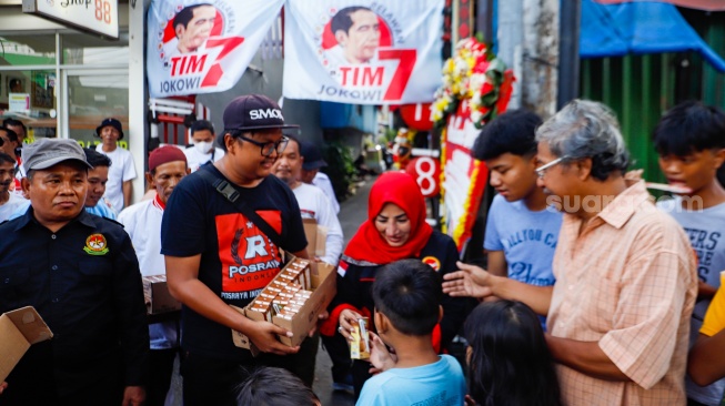 Relawan Jokowi membagikan susu kepada anak-anak di wilayah Menteng Wadas Timur, Jakarta, Selasa (30/4/2024). [Suara.com/Alfian Winanto]