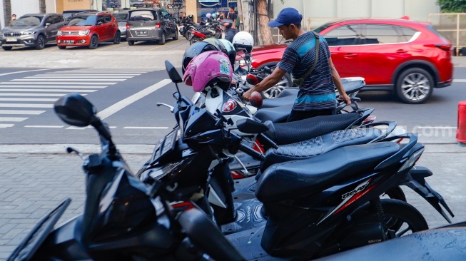 Aktivitas seorang juru parkir memarkirkan kendaraan di salah satu minimarket di kawasan Jakarta, Kamis (9/5/2024). [Suara.com/Alfian Winanto]