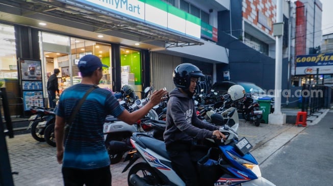 Aktivitas seorang juru parkir memarkirkan kendaraan di salah satu minimarket di kawasan Jakarta, Kamis (9/5/2024). [Suara.com/Alfian Winanto]