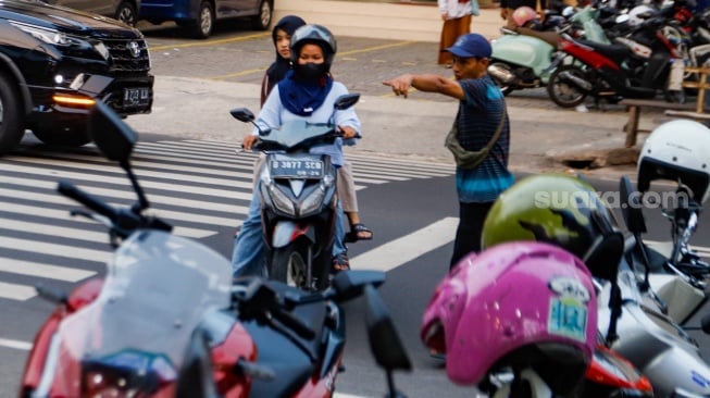 Aktivitas seorang juru parkir memarkirkan kendaraan di salah satu minimarket di kawasan Jakarta, Kamis (9/5/2024). [Suara.com/Alfian Winanto]