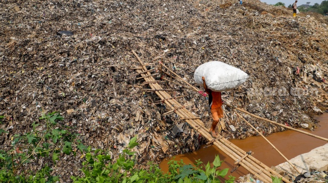 Warga membawa sampah daur ulang melewati lokasi longsor Tempat Pembuangan Akhir (TPA) Cipayung yang menimbun Kali Pesanggrahan di Depok, Jawa Barat, Senin (13/5/2024). [Suara.com/Alfian Winanto]