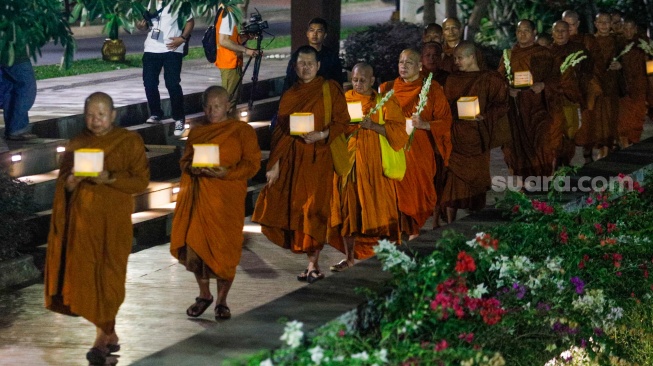 Para Bhikkhu berjalan sambil membawa lentera saat prosesi Walking Meditation di Taman Mini Indonesia Indah, Jakarta, Selasa (14/5/2024). [Suara.com/Alfian Winanto]