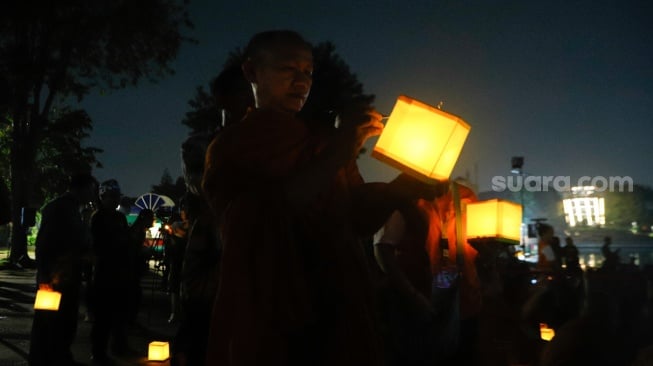 Seorang Bhikkhu menuliskan harapannya di lentera sebelum prosesi Larung Lentera Harapan Semesta di Taman Mini Indonesia Indah, Jakarta, Selasa (14/5/2024). [Suara.com/Alfian Winanto]