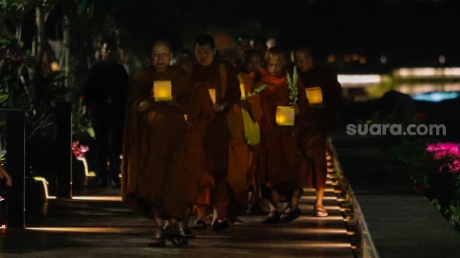 Para Bhikkhu berjalan sambil membawa lentera saat prosesi Walking Meditation di Taman Mini Indonesia Indah, Jakarta, Selasa (14/5/2024). [Suara.com/Alfian Winanto]