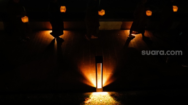 Para Bhikkhu berjalan sambil membawa lentera saat prosesi Walking Meditation di Taman Mini Indonesia Indah, Jakarta, Selasa (14/5/2024). [Suara.com/Alfian Winanto]