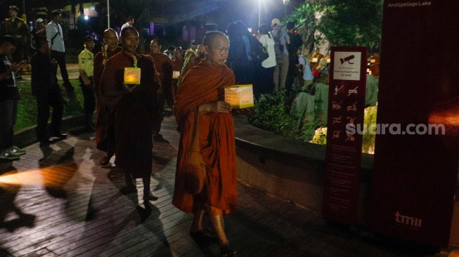 Para Bhikkhu berjalan sambil membawa lentera saat prosesi Walking Meditation di Taman Mini Indonesia Indah, Jakarta, Selasa (14/5/2024). [Suara.com/Alfian Winanto]