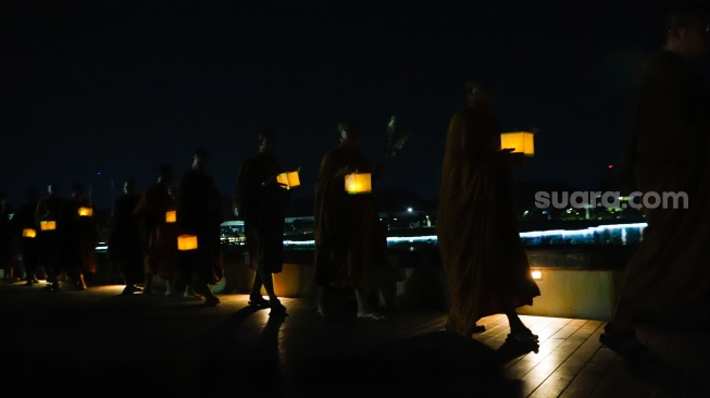 Para Bhikkhu berjalan sambil membawa lentera saat prosesi Walking Meditation di Taman Mini Indonesia Indah, Jakarta, Selasa (14/5/2024). [Suara.com/Alfian Winanto]