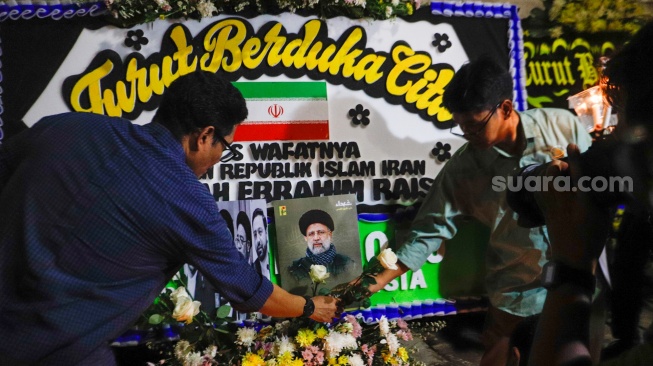 Warga meletakan bunga di tengah karangan bunga yang terpajang di depan Kantor Kedutaan Besar Iran, Jakarta, Senin (20/5/2024). [Suara.com/Alfian Winanto]