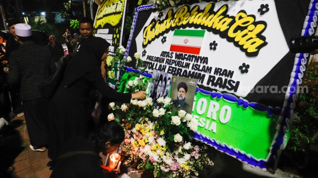 Warga meletakan bunga di tengah karangan bunga yang terpajang di depan Kantor Kedutaan Besar Iran, Jakarta, Senin (20/5/2024). [Suara.com/Alfian Winanto]