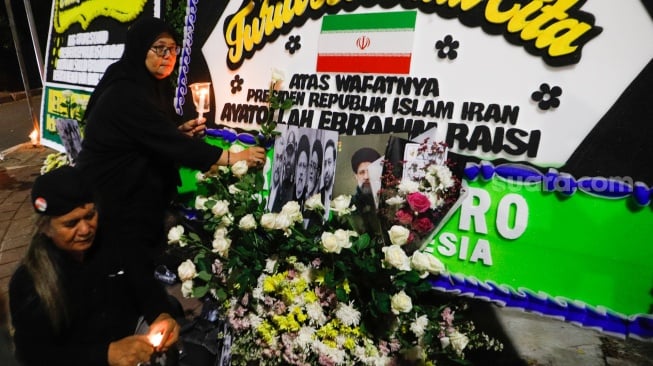 Warga meletakan bunga di tengah karangan bunga yang terpajang di depan Kantor Kedutaan Besar Iran, Jakarta, Senin (20/5/2024). [Suara.com/Alfian Winanto]