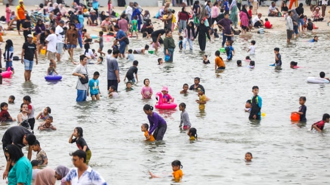 Pengunjung berwisata di Pantai Lagoon, Ancol Taman Impian, Jakarta, Minggu (26/5/2024). [Suara.com/Alfian Winanto]