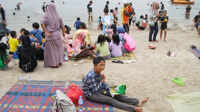 Pengunjung berwisata di Pantai Lagoon, Ancol Taman Impian, Jakarta, Minggu (26/5/2024). [Suara.com/Alfian Winanto]