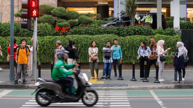 Pekerja melintas di pelican crossing di kawasan Perkantoran Sudirman, Jakarta, Selasa (28/5/2024). [Suara.com/Alfian Winanto]