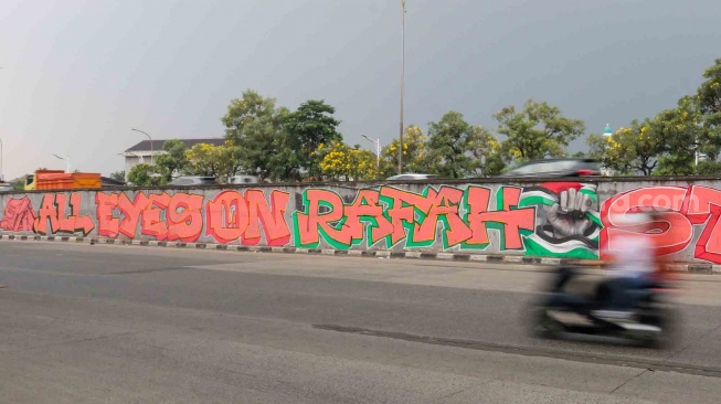 Pengendara melewati mural yang menggambarkan dukungan untuk warga Palestina di tembok pinggir tol lingkar luar Jakarta, Tanjung Barat, Jakarta Selatan, Senin (3/6/2024). [Suara.com/Alfian Winanto]