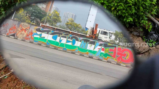 Pengendara melewati mural yang menggambarkan dukungan untuk warga Palestina di tembok pinggir tol lingkar luar Jakarta, Tanjung Barat, Jakarta Selatan, Senin (3/6/2024). [Suara.com/Alfian Winanto]