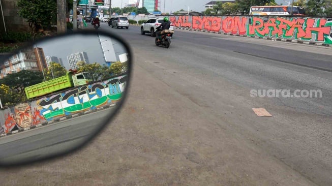 Pengendara melewati mural yang menggambarkan dukungan untuk warga Palestina di tembok pinggir tol lingkar luar Jakarta, Tanjung Barat, Jakarta Selatan, Senin (3/6/2024). [Suara.com/Alfian Winanto]