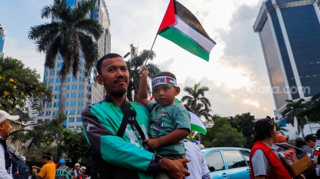 Seorang anak membawa bendera Palestina saat Aksi Bela Palestina di Kawasan Patung Kuda, Jakarta, Minggu (9/6/2024). [Suara.com/Alfian Winanto]