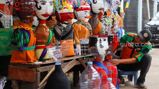 Petugas Unit Penanganan Sampah (UPS) Badan Air Dinas Lingkungan Hidup DKI Jakarta Kecamatan Jatinegara membuat ondel-ondel mini dari galon air minum bekas di Jakarta, Selasa (25/6/2024). [Suara.con/Alfian Winanto]