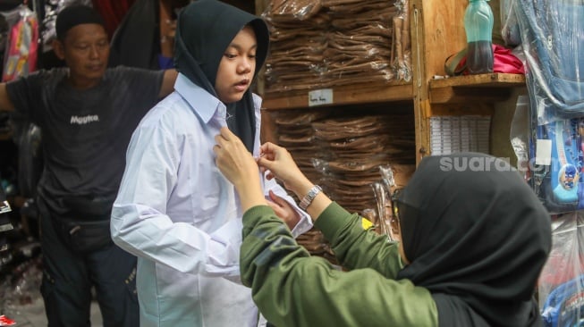 Warga mencoba seragam sekolah di Toko Seragam di Pasar Jatinegara, Jakarta, Selasa (2/7/2024). [Suara.com/Alfian Winanto]