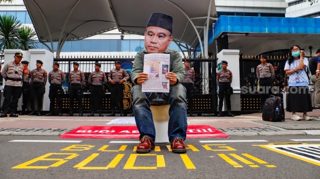 Seorang pengunjuk rasa duduk diatas closet memakai topeng wajah Menkominfo Budi Arie Setiadi saat menggelar aksi di depan gedung Kementerian Komunikasi dan Informatika (Kemenkominfo) di Jakarta, Rabu (10/7/2024). [Suara.com/Alfian Winanto]