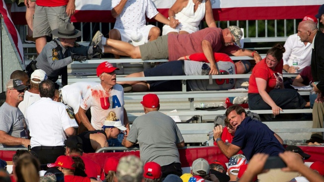 Pendukung Trump terlihat berlumuran darah dan berlindung di tribun setelah insiden penembakan kepada kandidat Partai Republik dan mantan Presiden AS Donald Trump pada acara kampanye di Butler Farm Show Inc. di Butler, Pennsylvania, Sabtu (13/7/2024). [Rebecca DROKE/AFP]