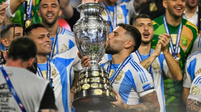 Bek Argentina Nicolas Otamendi mencium trofi saat ia merayakan kemenangan pertandingan sepak bola final Copa America 2024 antara Argentina dan Kolombia di Stadion Hard Rock, di Miami, Florida, Minggu (14/7/2024). [Chandan Khanna / AFP]