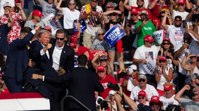 Kandidat Partai Republik dan mantan Presiden AS Donald Trump terlihat dengan wajah berlumuran darah dikelilingi oleh agen Secret Service dan dibawa turun dari panggung usai insiden penembakan pada acara kampanye di Butler Farm Show Inc. di Butler, Pennsylvania, Sabtu (13/7/2024). [Rebecca DROKE/AFP]