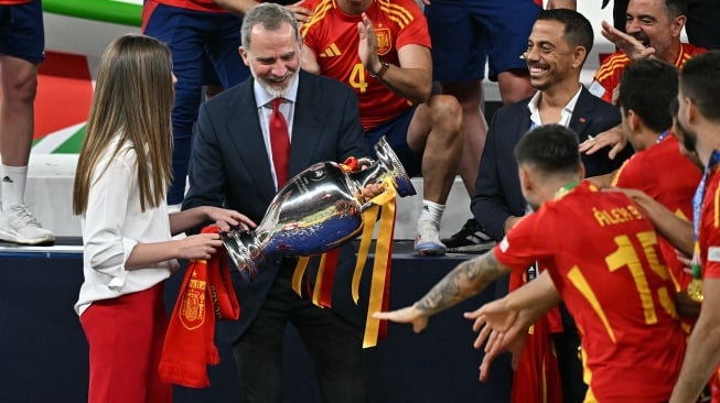 Raja Spanyol Felipe VI (tengah) didampingi putrinya, Putri Sofia memegang trofi dan berselebrasi bersama para pemain Spanyol setelah pertandingan sepak bola Final Euro 2024 antara Spanyol dan Inggris di Olympiastadion, Berlin, Jerman, Minggu (14/7/2024). [JAVIER SORIANO / AFP]