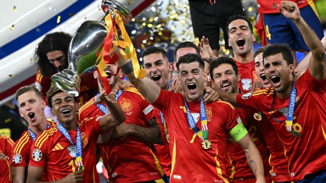 Penyerang Spanyol Alvaro Morata (tengah) mengangkat trofi di samping gelandang Spanyol Rodri (kanan) dan penyerang Spanyol Lamine Yamal (kiri) setelah memenangkan pertandingan sepak bola Final Euro 2024 antara Spanyol dan Inggris di Olympiastadion, Berlin, Jerman, Minggu (14/7/2024). [JAVIER SORIANO / AFP]