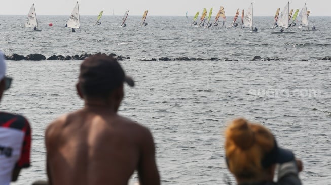 Pengunjung menonton atlet layar beradu kecepatan saat mengikuti pertandingan Jakarta International Sailing Championship 2024 di area Symphony of The Sea, Ancol, Jakarta, Jumat (26/7/2024). [Suara.com/Alfian Winanto]
