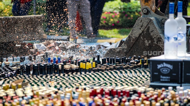 Petugas melakukan pemusnahan minuman keras ilegal hasil penindakan di Kantor Pusat Bea Cukai, Jakarta, Rabu (31/7/2024). [Suara.com/Alfian Winanto]