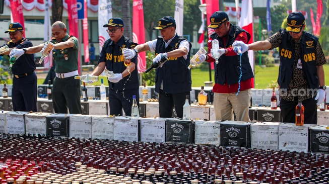 Petugas melakukan pemusnahan minuman keras ilegal hasil penindakan di Kantor Pusat Bea Cukai, Jakarta, Rabu (31/7/2024). [Suara.com/Alfian Winanto]