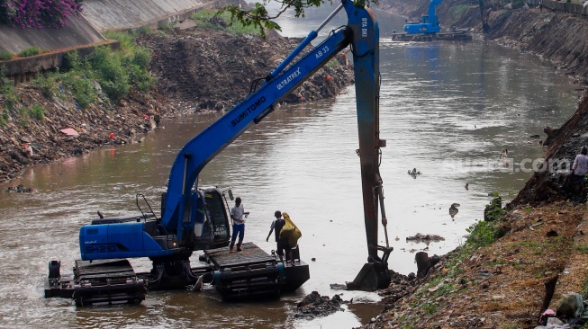 Pekerja menggunakan alat berat mengeruk lumpur endapan Kali Ciliwung di kawasan Manggarai, Jakarta, Kamis (8/8/2024). [Suara.com/Alfian Winanto]