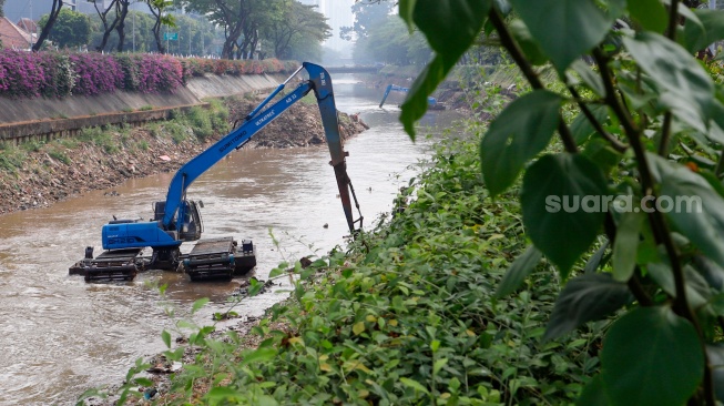 Pekerja menggunakan alat berat mengeruk lumpur endapan Kali Ciliwung di kawasan Manggarai, Jakarta, Kamis (8/8/2024). [Suara.com/Alfian Winanto]