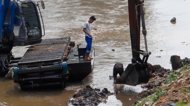Pekerja menggunakan alat berat mengeruk lumpur endapan Kali Ciliwung di kawasan Manggarai, Jakarta, Kamis (8/8/2024). [Suara.com/Alfian Winanto]