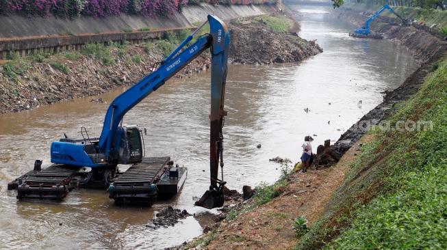 Pekerja menggunakan alat berat mengeruk lumpur endapan Kali Ciliwung di kawasan Manggarai, Jakarta, Kamis (8/8/2024). [Suara.com/Alfian Winanto]