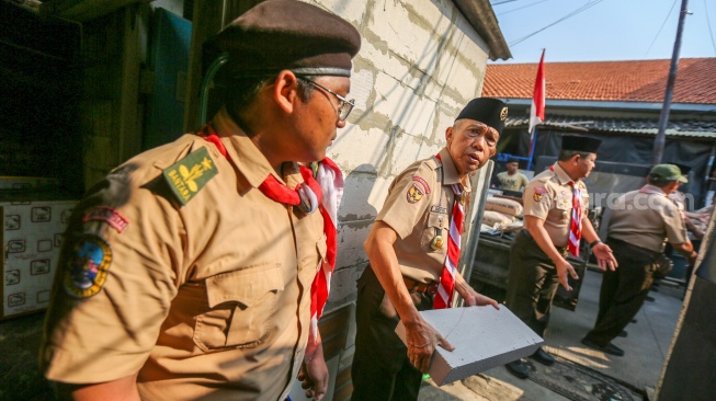 Anggota Kwarnas Pramuka membantu memasukkan bahan bangunan untuk bedah rumah warga saat kegiatan bakti sosial pramuka di Kebon Bawang, Jakarta Utara, Jumat (9/8/2024). [Suara.com/Alfian Winanto]