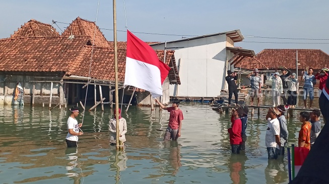 Warga Dukuh Timbulsloko, Desa Timbulsloko, Kecamatan Sayung, Kabupaten Demak, melaksanakan upacara HUT ke-79 RI di atas rob, Sabtu (17/08/2024). (suara.com/Sigit AF)