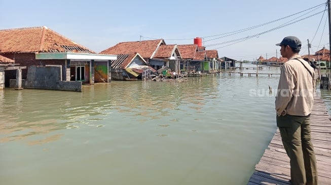 Seseorang memandang deretan rumah kosong di Dukuh Timbulsloko, Desa Timbusloko, Kecamatan Sayung, Kabupaten Demak, Jawa Tengah, Selasa (20/08/2024). (suara.com/Sigit AF)