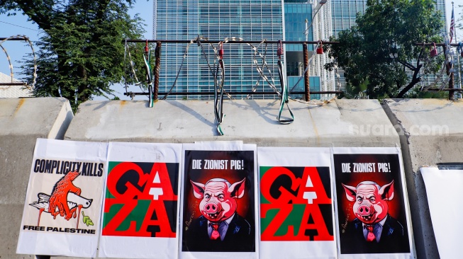 Gembok dan poster berisi kritikan terpasang di tembok berduri saat aksi bela Palestina di depan Kedutaan Besar Amerika, Jakarta, Jumat (30/8/2024). [Suara.com/Alfian Winanto]