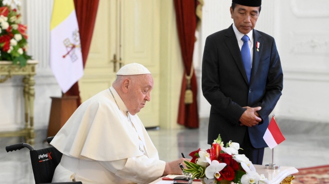 Paus Fransiskus (kiri) menyanyikan sebuah buku didampingi Presiden Indonesia Joko Widodo di Istana Kepresidenan, Jakarta, Rabu (4/9/2024). [Handout / VATICAN MEDIA / AFP]
