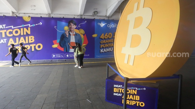 Warga melintas dengan latar logo Bitcoin di Terowongan Kendal, Jakarta, Selasa (24/9/2024). [Suara.com/Alfian Winanto]